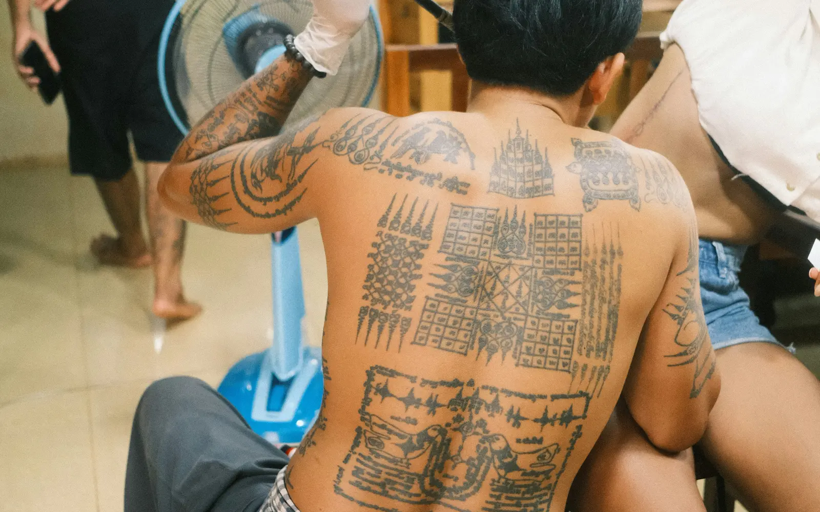 Man with stick and poke tattoo on back, sitting in chair